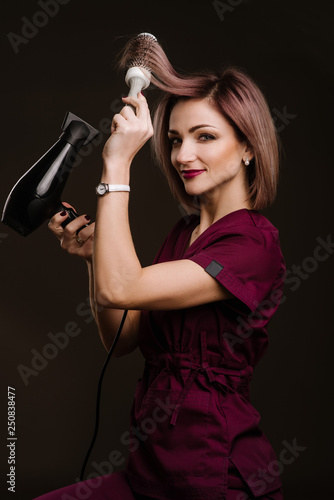 A woman hairdresser posing with hairdryer in studio on the black background