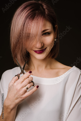 Woman hairdresser posing with a scissors on black background