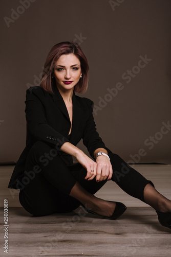 Successful business woman in strict black suit posing in studio