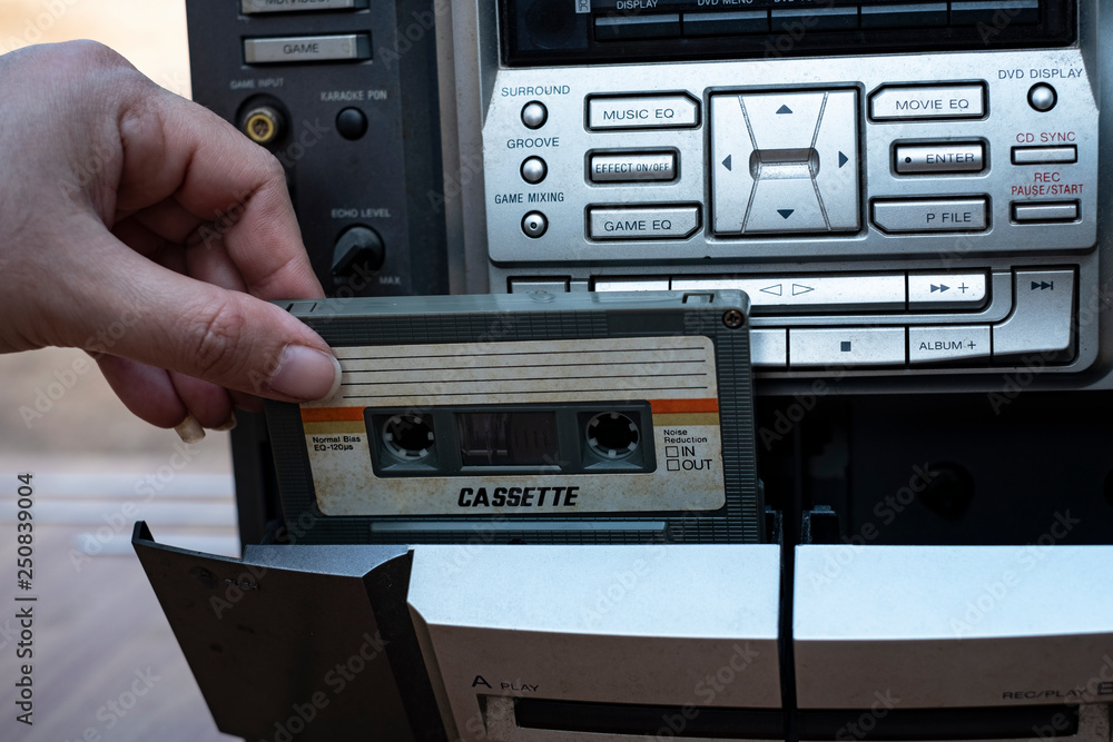 Fototapeta premium Women hand putting cassette into old fashioned audio tape player on top desk wood background