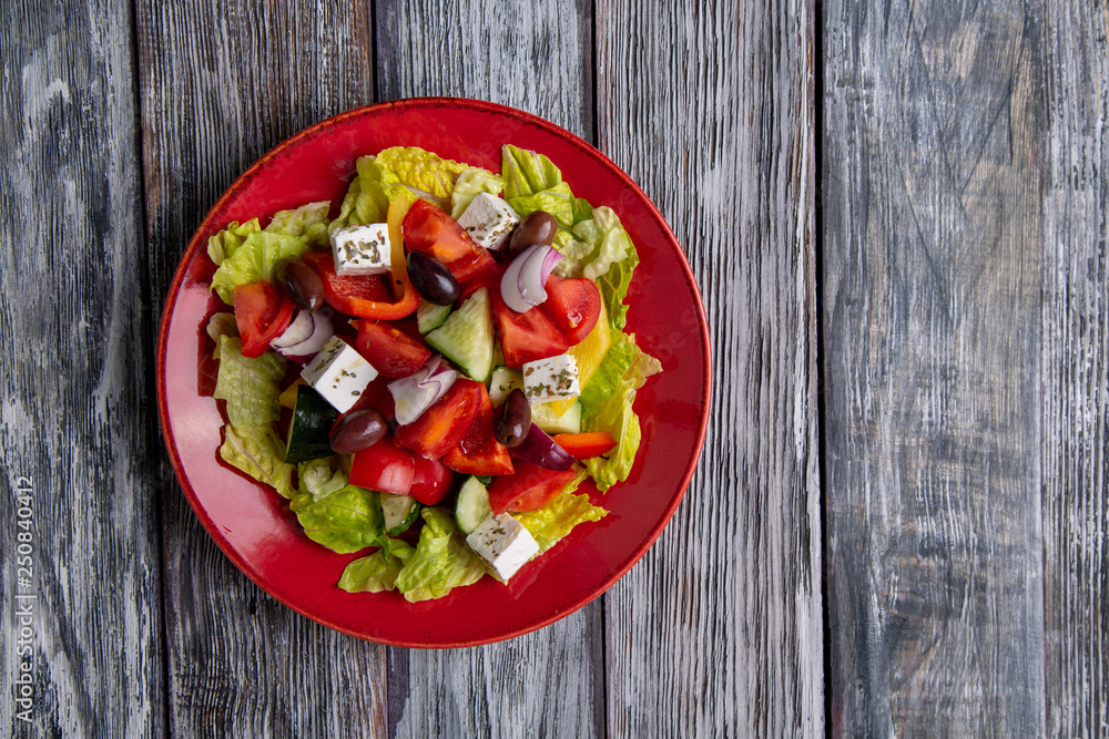 Greek salad of fresh cucumber, tomato, sweet pepper, lettuce, red onion, feta cheese and olives with olive oil on wooden background. Healthy food