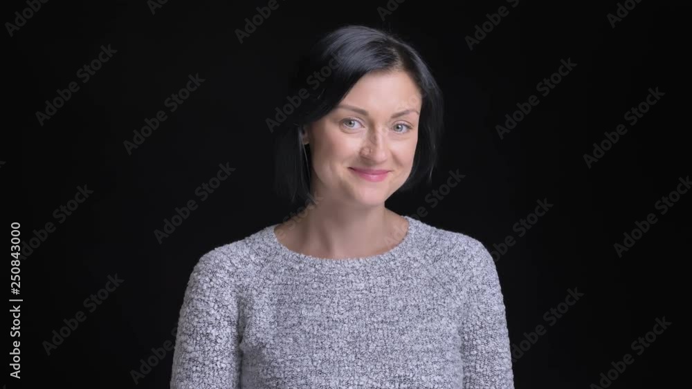 Closeup portrait of adult beautiful caucasian female with short black hair getting shy and awkward smiling while looking straight at camera Closeup portrait of adult beautiful caucasian female with short black hair getting shy and awkward smiling while looking straight at camera