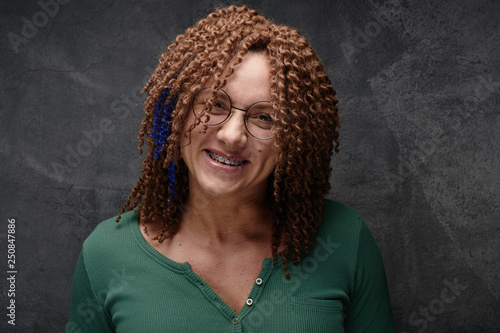 Portrait of a laughing authentic adult woman with afro curls and brequits against a black wall in the studio. Unusual stylish woman with red hair photo