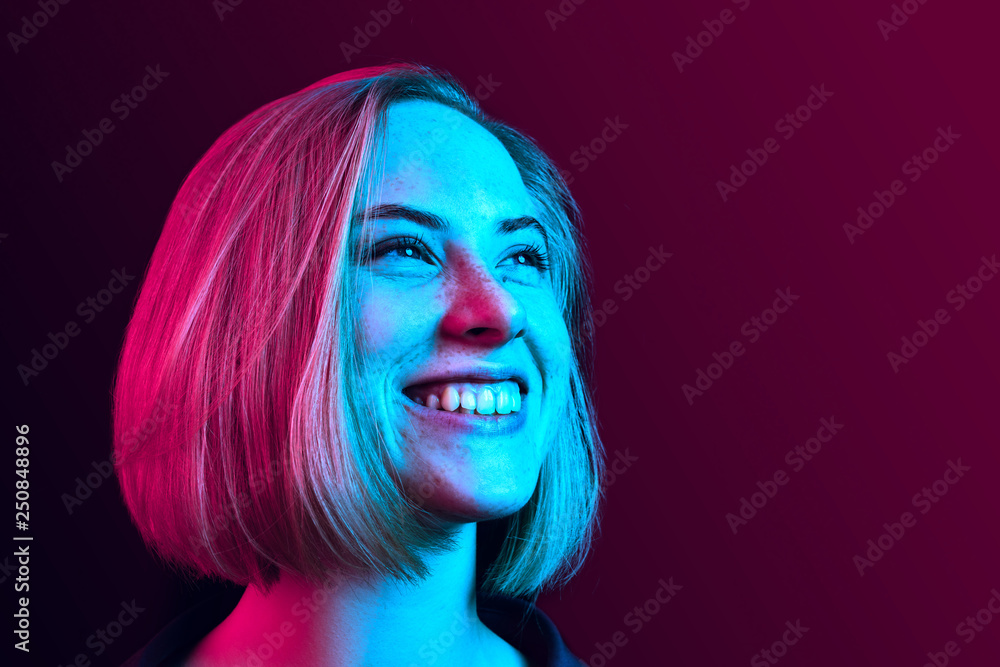 Happy business woman standing and smiling on neon studio background. Beautiful female half-length portrait. Young emotional woman. The human emotions, facial expression concept - obrazy, fototapety, plakaty 