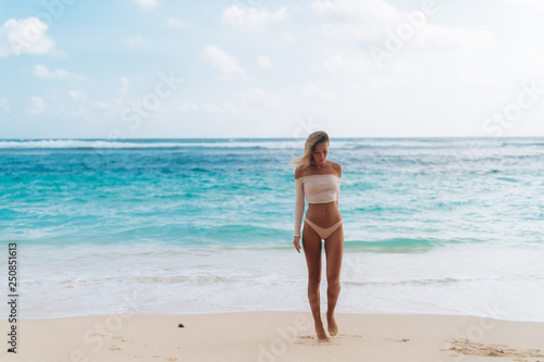 Beautiful tanned girl standing on beach with white sand and blue ocean © romannoru