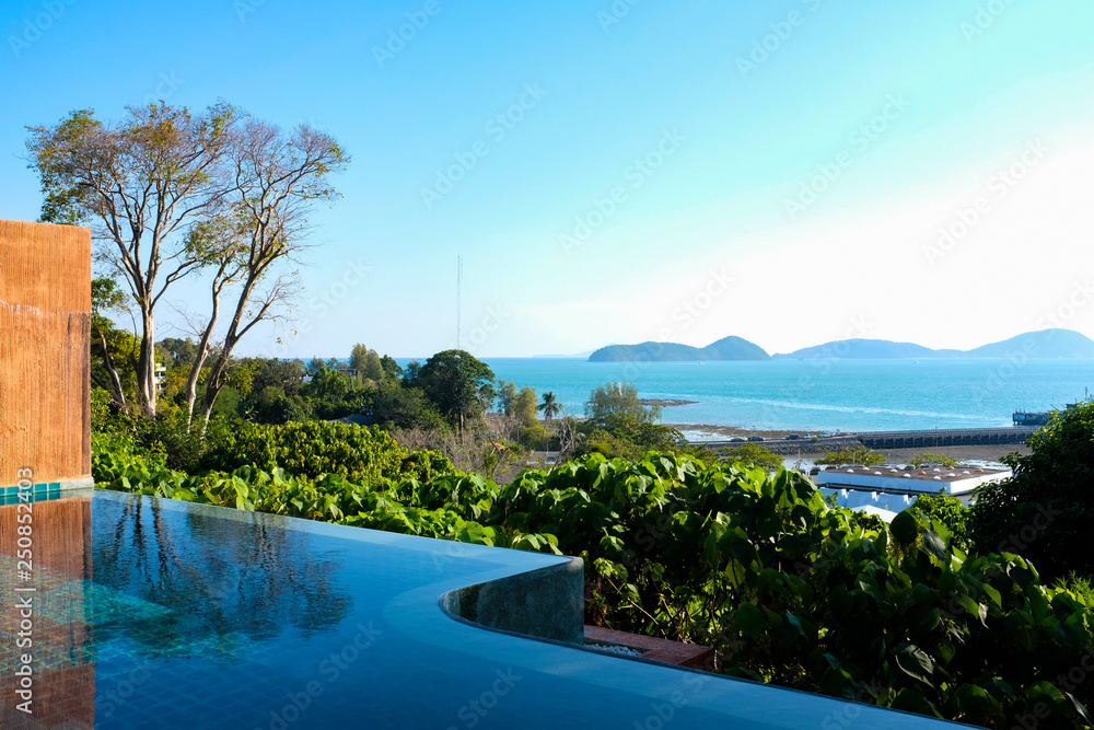 View from an infinity pool outside tropical villa resort with blue sea in background and bright blue sky