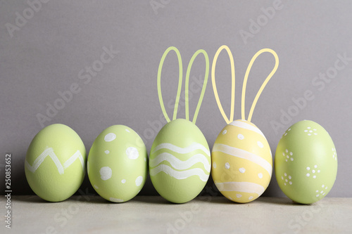 Set of painted eggs with Easter bunny ears on table against grey background
