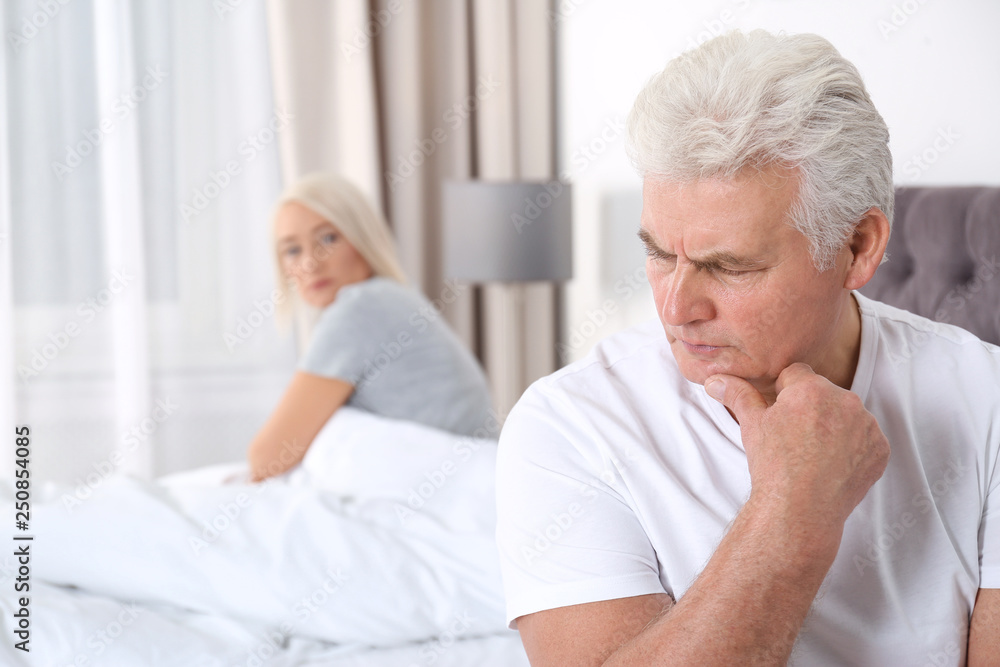 Upset mature couple with relationship problems sitting on bed at home Upset mature couple with relationship problems sitting on bed at home