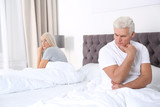 Upset mature couple with relationship problems sitting on bed at home
