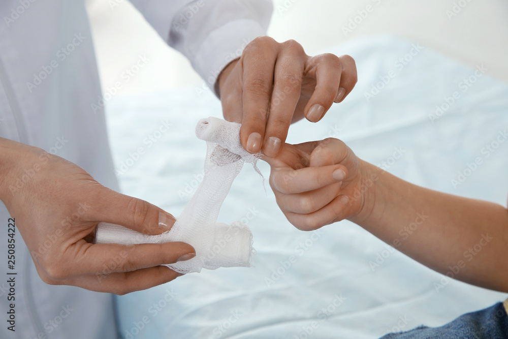 Female doctor applying bandage on little child's finger in clinic, closeup. First aid Female doctor applying bandage on little child's finger in clinic, closeup. First aid