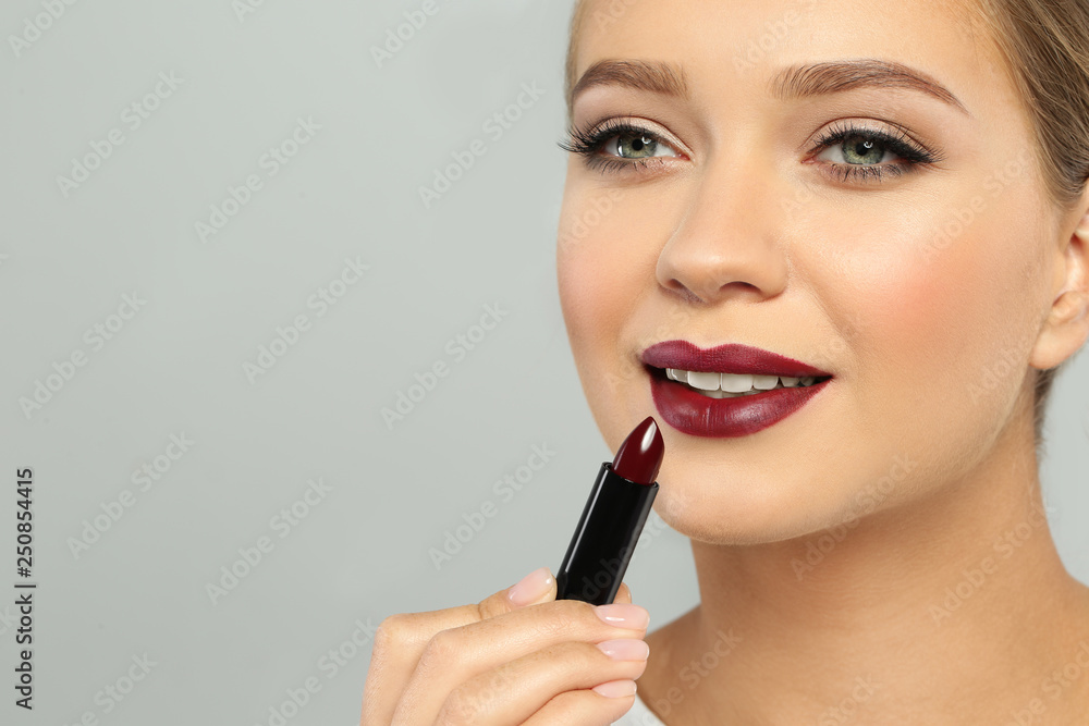 Beautiful woman applying dark lipstick on gray background. Space for text Beautiful woman applying dark lipstick on gray background. Space for text