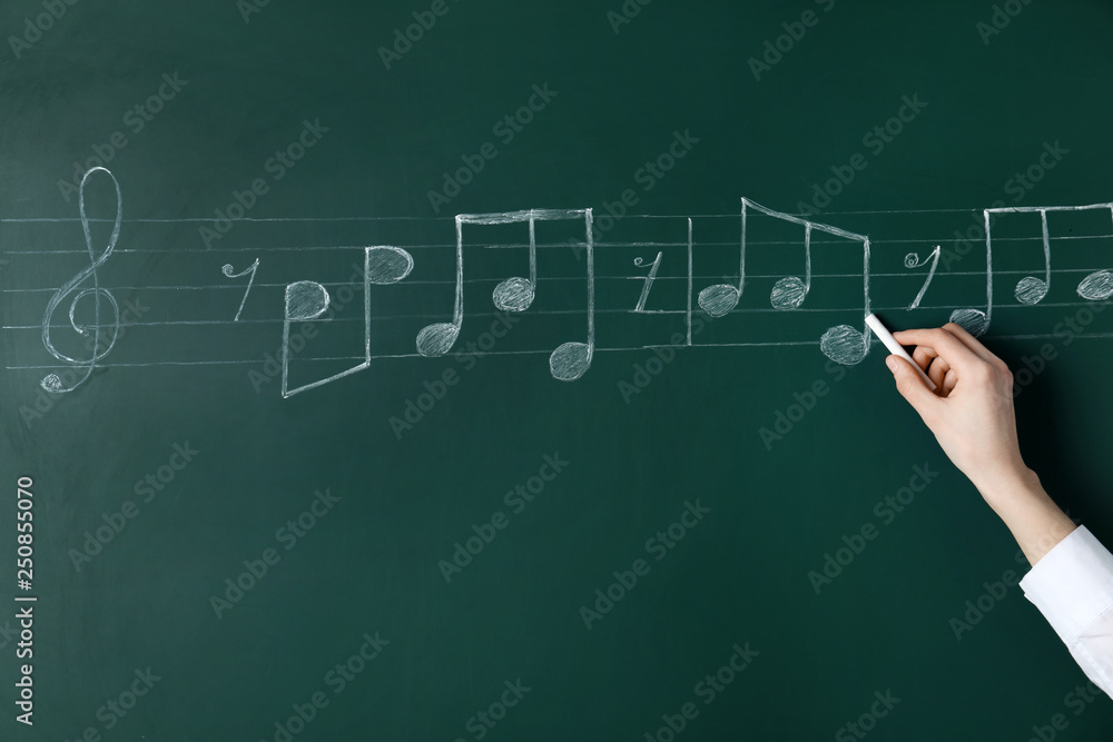 Woman writing music notes with chalk on blackboard, closeup Woman writing music notes with chalk on blackboard, closeup