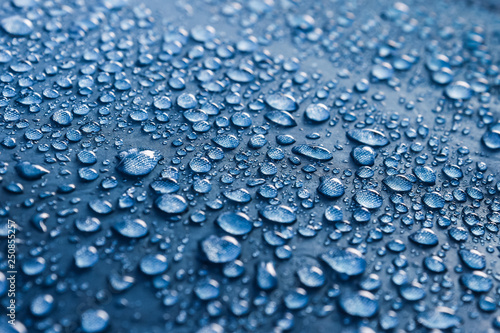 Water drops on the fabric. Rain Water droplets on blue fiber waterproof fabric. Water drops pattern over a waterproof cloth. Blue background. Dark blue rainproof tent sheet with morning rain drops.