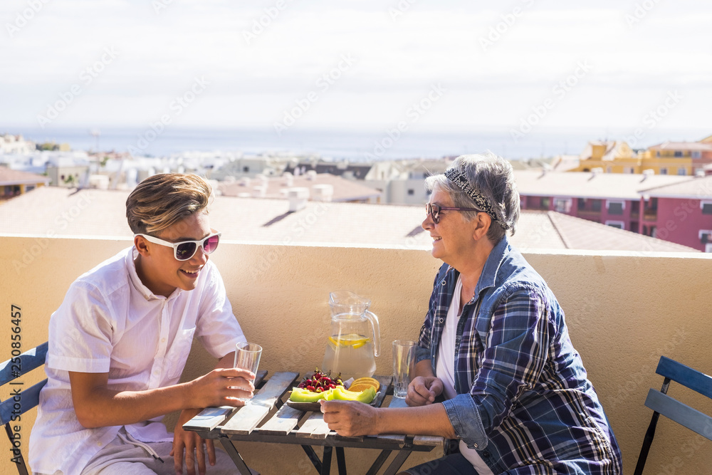 happy leisure activity on the terrace rooftop having breakfast with smiles and happiness for grandmother and teenager family caucasian people. ocean and buildings view, outdoor coule together