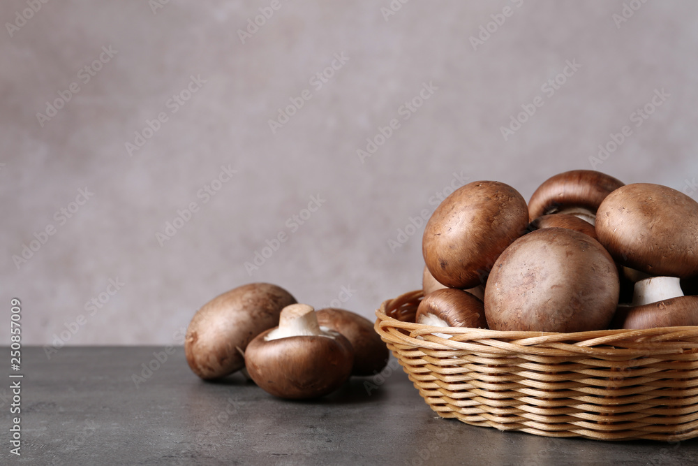 Wicker bowl and fresh champignon mushrooms on table against color background. Space for text Wicker bowl and fresh champignon mushrooms on table against color background. Space for text
