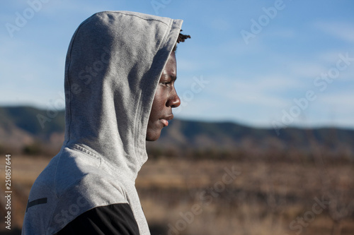 chico africano con sudadera gris y capucha puesta en un entorno natural con cielo azul y día soleado photo