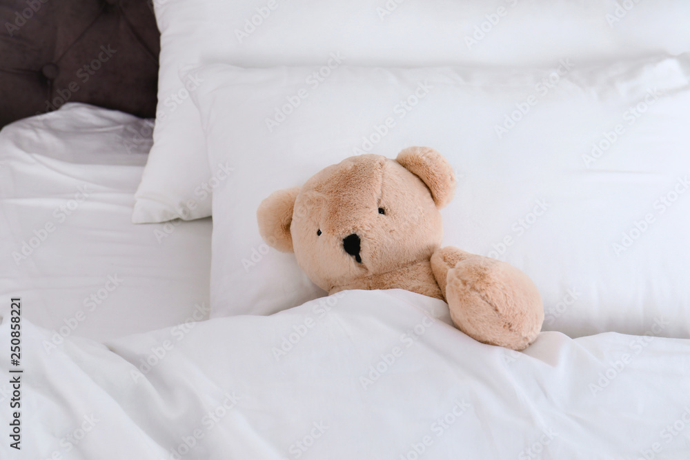 Cute teddy bear lying in bed indoors. Space for text