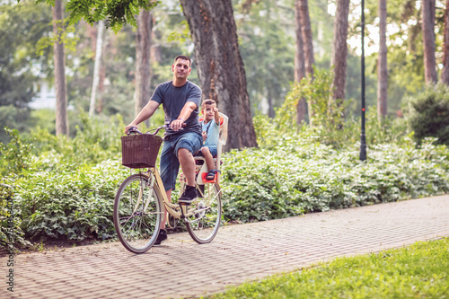 Happy Dad and son riding bicycles outdoors in a city park.