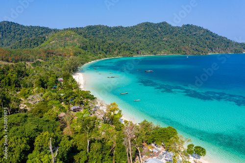 Aerial drone view of traditional fishing boats moored over a coral reef around a remote, green tropical island in the Mergui Archipelago