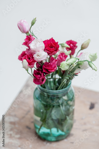 Bouquet of red Eustoma in glass jar on white background