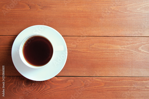 White cup with tea on a saucer. On a wooden brown background.