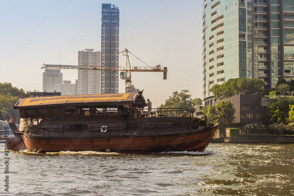 Traditional wooden boat with restaurant on the Chao Phraya river cruising tour. River view of the tourist boat takes visitors for sightseeing tour in Bangkok along the Chao Phraya River.