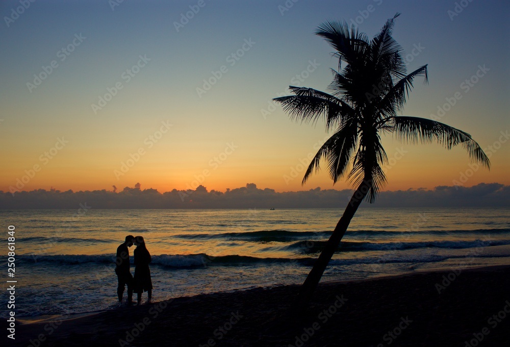 couple on beach near palm tree at sunrise