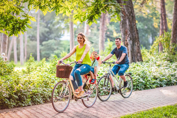 Happy family is riding bikes outdoors .