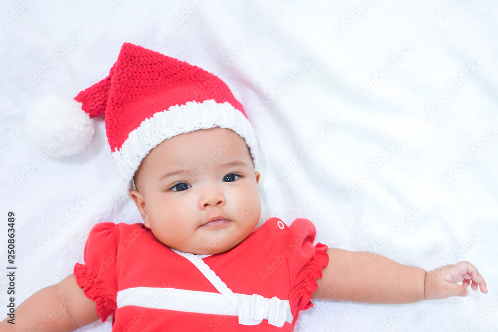 Asian newborn baby is wearing red dress and knitting Christmas hat on white towel background. A baby is ready for Christmas party. Asian newborn baby is wearing red dress and knitting Christmas hat on white towel background. A baby is ready for Christmas party.