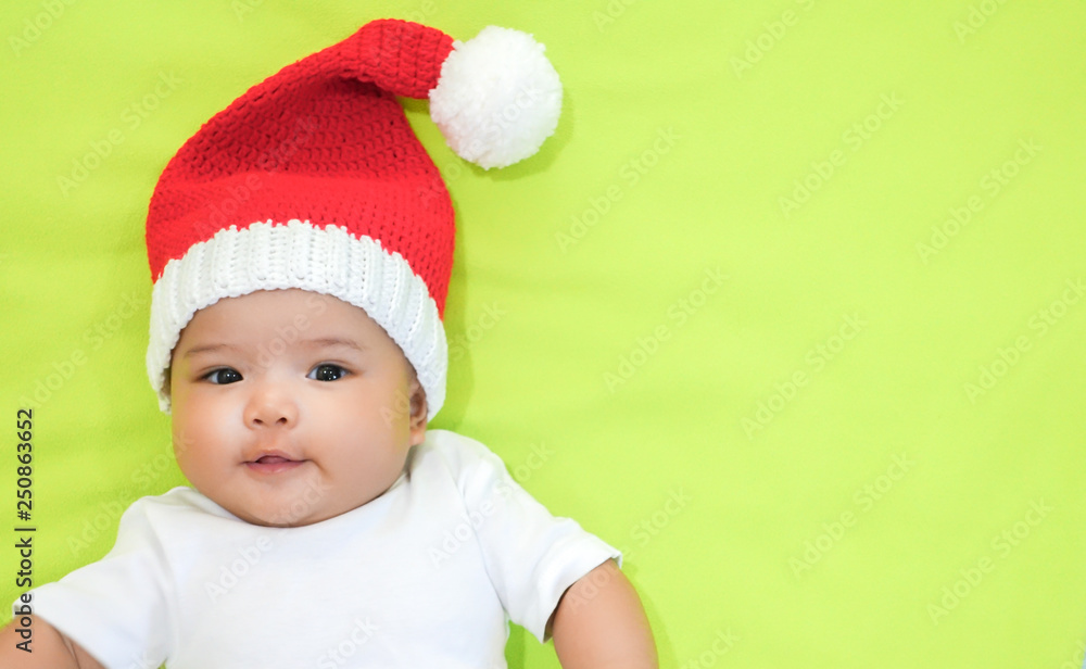 Newborn Asian baby is wearing red Christmas knitting hat and white dress on light green background Newborn Asian baby is wearing red Christmas knitting hat and white dress on light green background