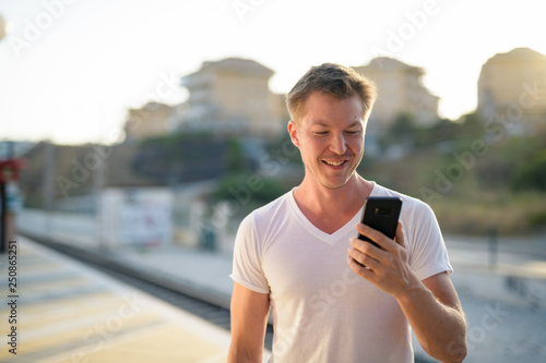 Young Happy Tourist Man Smiling While Using Phone At The Train Station