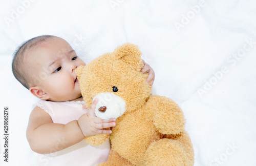 Asian baby hug her brown bear doll on white background. Baby girl loves her bear doll friend.