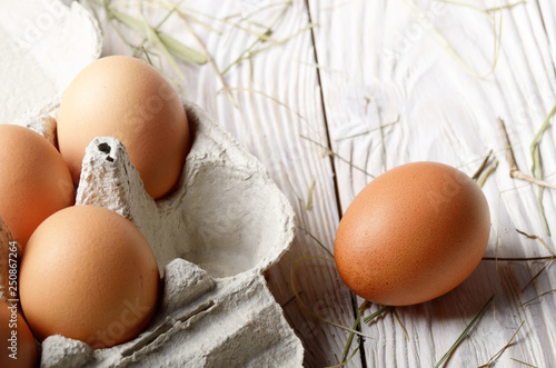 Raw organic brown chicken eggs in eco friendly paper carton on white kitchen wooden table photo