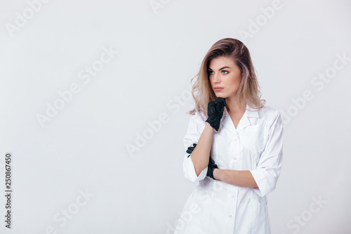Portrait of young female professional cosmetologist in black gloves thinking. Woman beautician doctor in studio. copy spacce