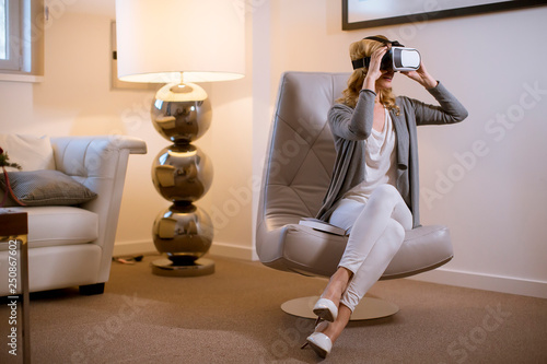 Joyful young woman playing computer games with virtual reality googles at home