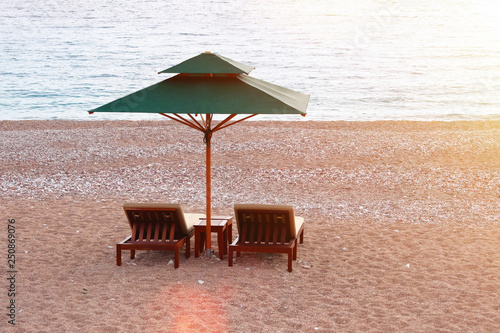 Lounge chairs with sun umbrella on beach. Perfect vacation concept. Blue sea and sky with soft yellow sunlight on background. Rest with comfort.