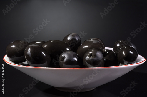 Bowl of black olives against a dark background.