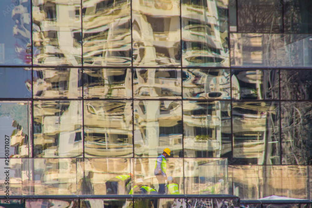 Modern skyscraper building with glass reflecting the workers in construction site. Abstract reflection of the office building with construction worker.