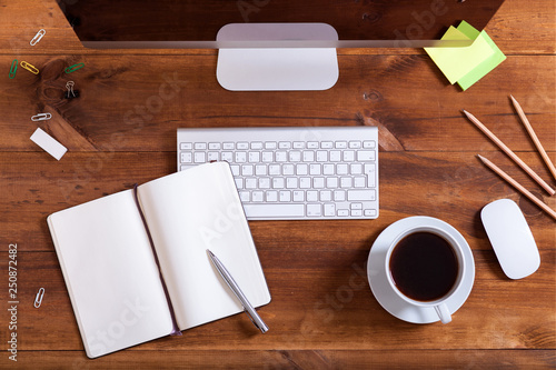 Workplace background  top above view of desk with desktop computer monitor keyboard open notebook with pen and coffee on brown wooden table  office supplies and business equipment for work concept