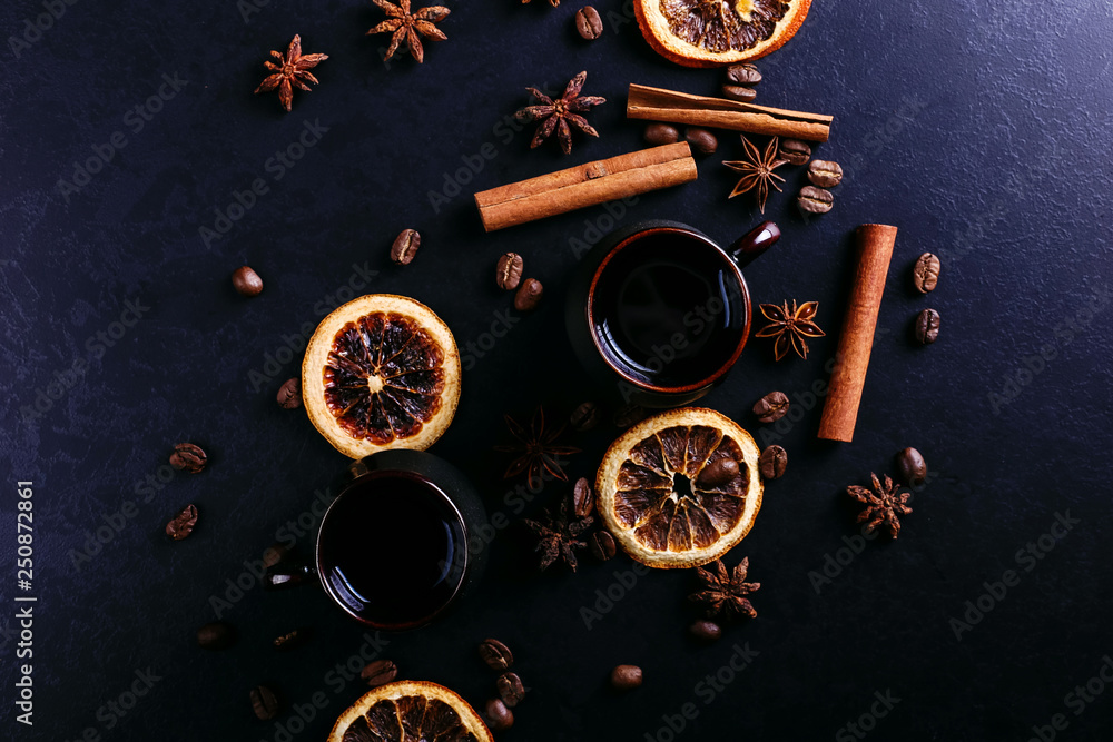 A cup of coffee, star anise, cinnamon, dried orange and coffee beans on a dark kitchen countertop. Fragrant spices for a drink, close-up, top view, flat ley.