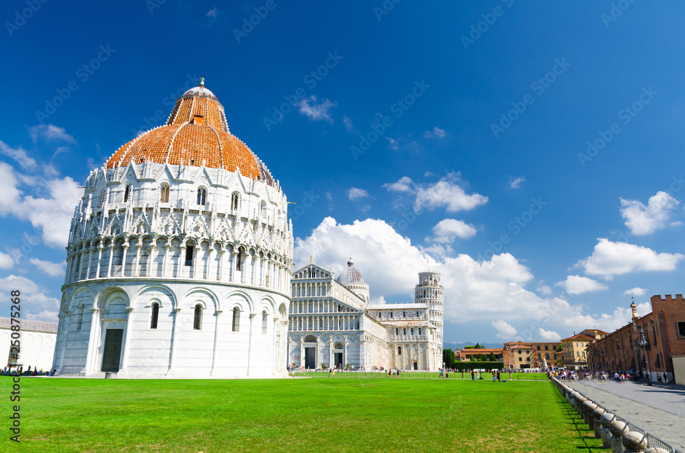 Pisa Baptistery Battistero, Pisa Cathedral Duomo Cattedrale and Leaning Tower Torre on Piazza del Miracoli square green grass lawn, blue sky with white clouds background in sunny day, Tuscany, Italy