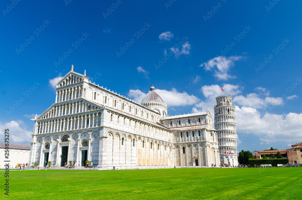Pisa Cathedral Duomo Cattedrale and Leaning Tower Torre on Piazza del Miracoli square green grass lawn, blue sky with white clouds copy space background in sunny day, Tuscany, Italy
