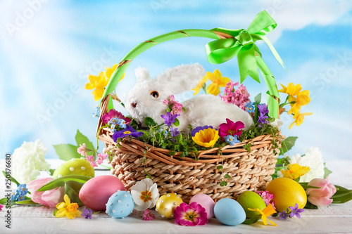 Easter composition with bunny in basket, spring flowers and colorful Easter eggs .