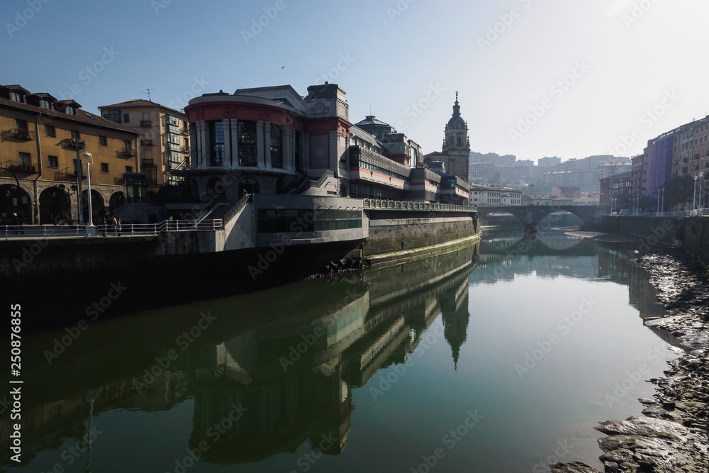 Naklejka premium The Ribera market and the church of San Anton of Bilbao seen from the river