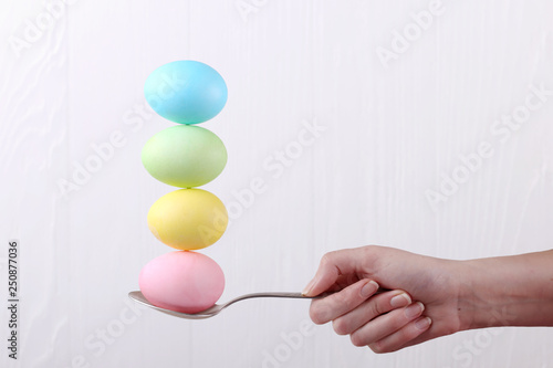 Female hand holds a spoon on which multi-colored eggs are balanced, on a white background. Unusual design, Easter concept, copy space.