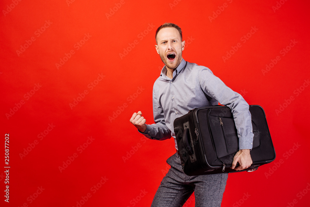 young male tourist standing with black suitcase on red background young male tourist standing with black suitcase on red background