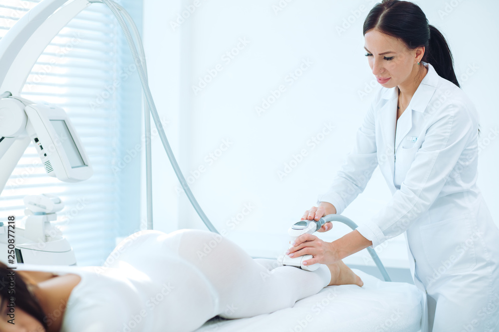 Fototapeta premium RF lifting massage, Close up of cosmetologist doctor hands manipulating with hardware cosmetological gadget. Slimming belly and abdomen area. Slender body shaping.