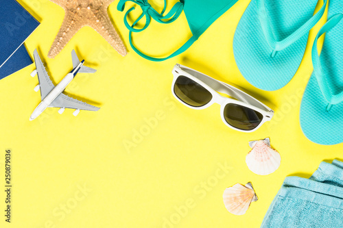 Blue flip flops, sunglasses, passport, plane and starfish on yellow background.