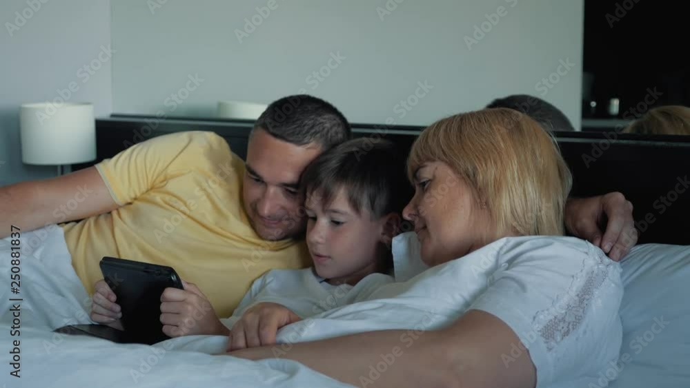 A happy family with one child lying on the bed and using a digital tablet and smartphones. Modern technologies of virtual life A happy family with one child lying on the bed and using a digital tablet and smartphones. Modern technologies of virtual life