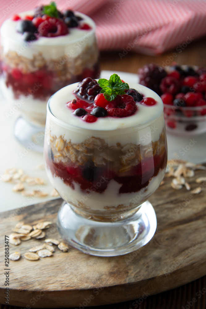 Glass jar withovernight oats, granola and yogurt with berry, raspberries and blackberries on wooden cutting board over wooden background. Healthy food. Glass jar withovernight oats, granola and yogurt with berry, raspberries and blackberries on wooden cutting board over wooden background. Healthy food.